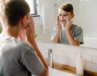 Young Boy Washing Face With Soap In Bathroom Mirror