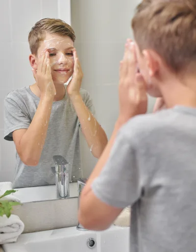 Young Boy Washing Face With Soap In Bathroom Mirror
