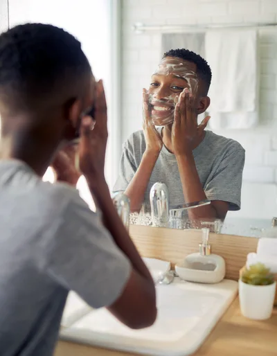 Young Black Man Washing Face With Cleanser In Bathroom