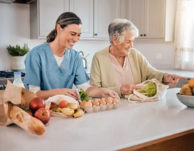 Caregiver Helping Senior Woman Unpack Groceries In Kitchen