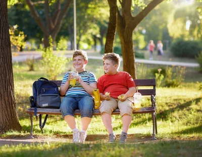Two Young Boys Eating Snacks on a Park Bench