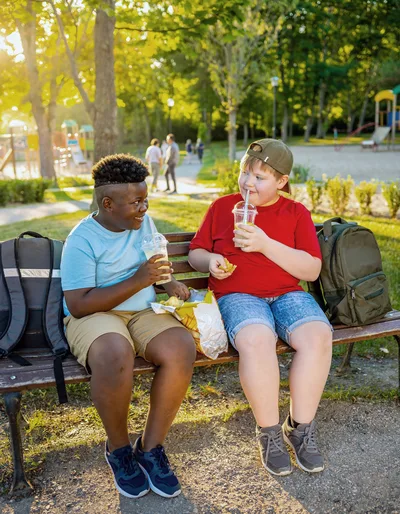 Two Boys Eating Snacks and Drinking Lemonade on Park Bench