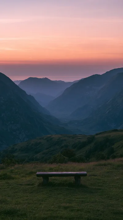 Wooden Bench Overlooking A Mountain Valley At Sunset