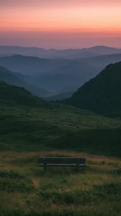 Wooden Bench Overlooking A Mountain Valley At Sunset