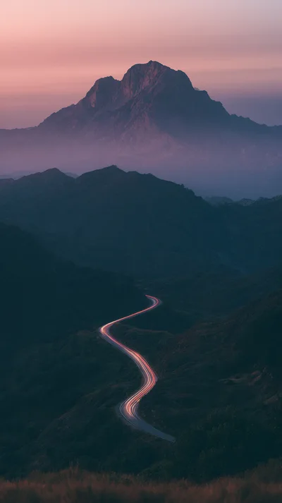 Winding Mountain Road With Car Light Trails At Sunset