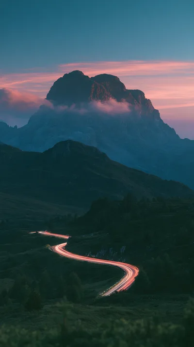 Winding Mountain Road With Car Light Trails At Sunset