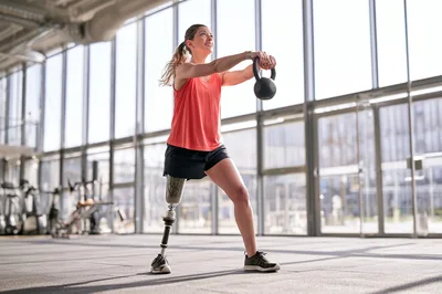 Amputee Woman Exercising With Kettlebell In Modern Gym