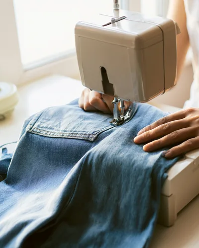 Person Sewing Denim Jeans With A Sewing Machine