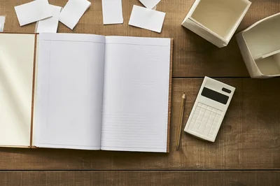 Open Notebook With Calculator And Pencil On Wooden Desk