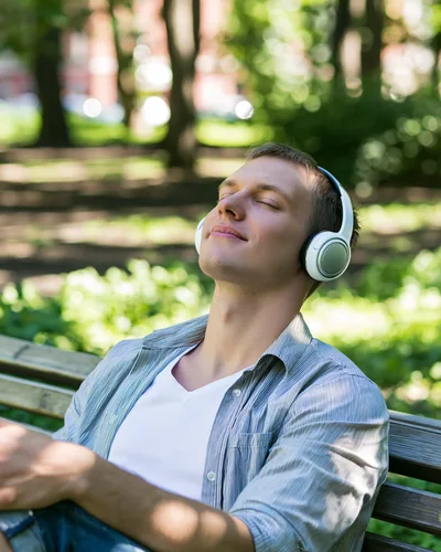 Young Man Relaxing With Headphones On Park Bench