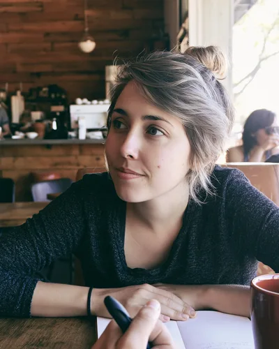 Young Woman Sitting At Cafe Table With Notebook