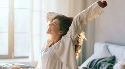 Young Woman Stretching In Bed During Morning Sunlight