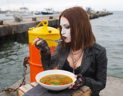 Goth Woman Eating Soup At A Harbor Pier
