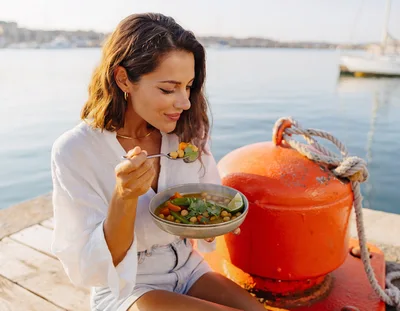Woman Eating Healthy Chickpea Soup By The Harbor