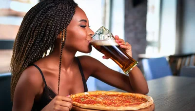Young Woman Drinking Beer With Pizza In Restaurant
