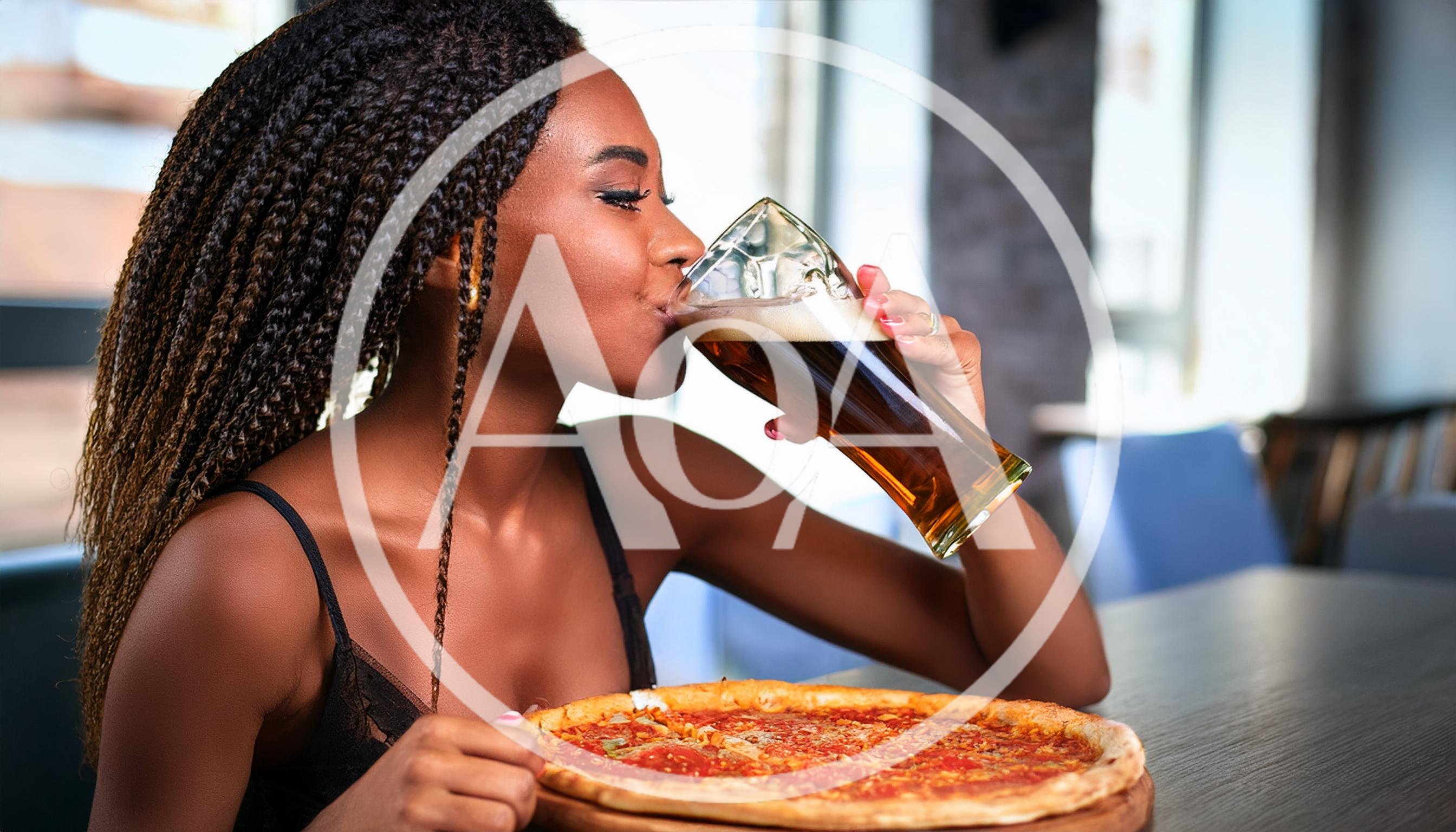 Young Woman Drinking Beer With Pizza In Restaurant