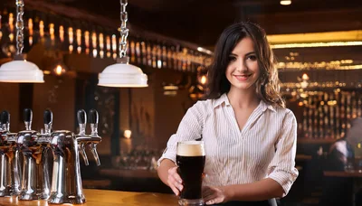 Smiling Female Bartender Serving A Pint Of Stout Beer