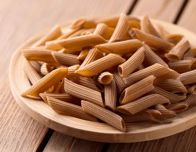 Whole Wheat Penne Pasta On A Wooden Plate