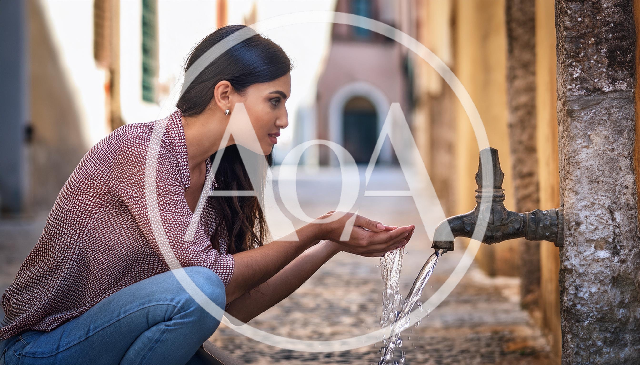 Young Woman Cupping Hands Under Outdoor Water Fountain