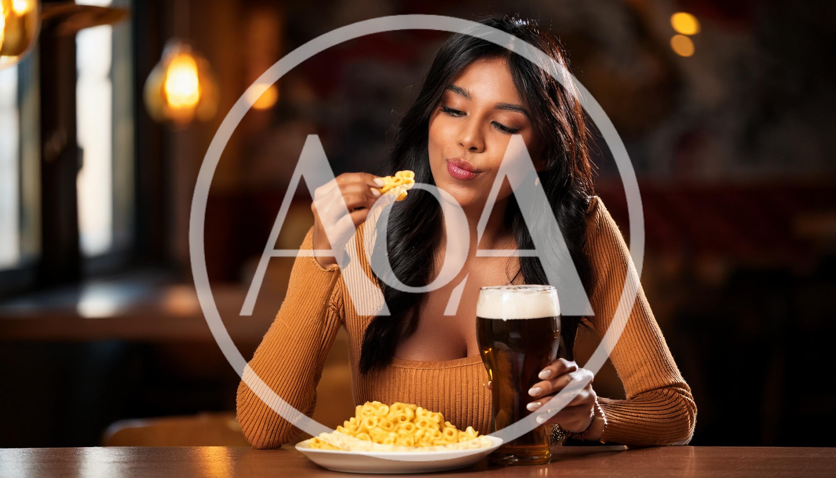 Young Woman Eating Pasta And Drinking Beer In Restaurant