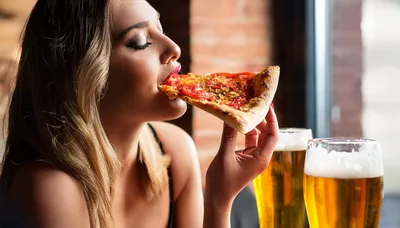 Young Woman Eating Pizza Slice With Beer