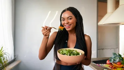 Young Woman Eating Fresh Salad In Kitchen