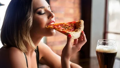 Young Woman Eating Pizza Slice In A Restaurant