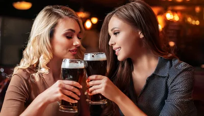 Two Young Women Toasting With Dark Beer Glasses