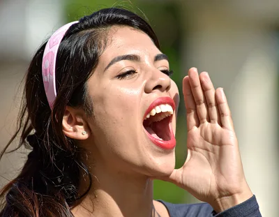 Young Hispanic Woman Shouting With Hand Near Mouth
