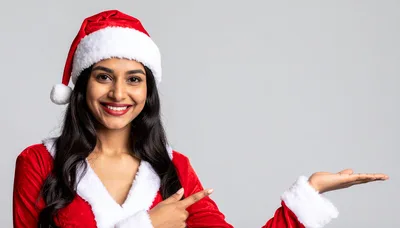 Young Woman In Santa Costume Pointing At Empty Space