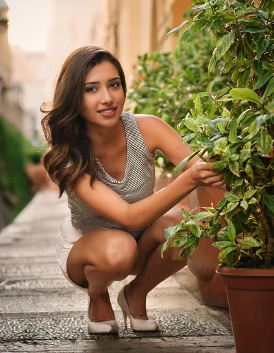 Young Woman Crouching Beside Potted Plants Outdoors
