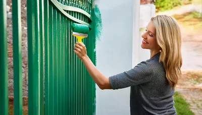 Woman Painting A Green Metal Gate With A Roller