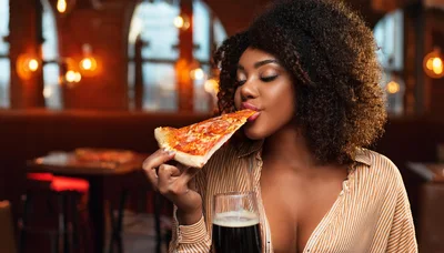 Young Woman Eating Pizza Slice In A Restaurant