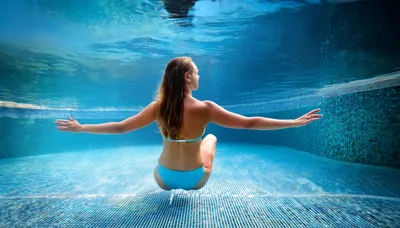 Woman Swimming Underwater In A Blue Tiled Pool