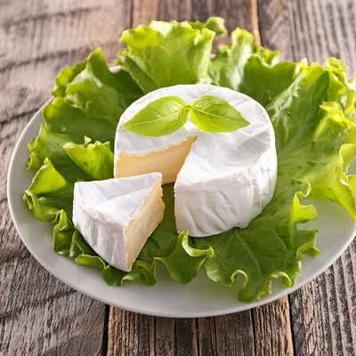 Camembert Cheese Wheel With A Slice On Lettuce