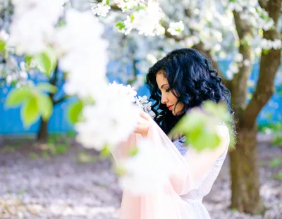 Woman With Curly Hair Posing In Blooming Apple Orchard