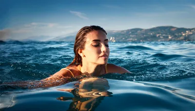 Young Woman Swimming In The Ocean At Sunset