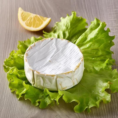 Round Brie Cheese Wheel on Fresh Lettuce Leaves