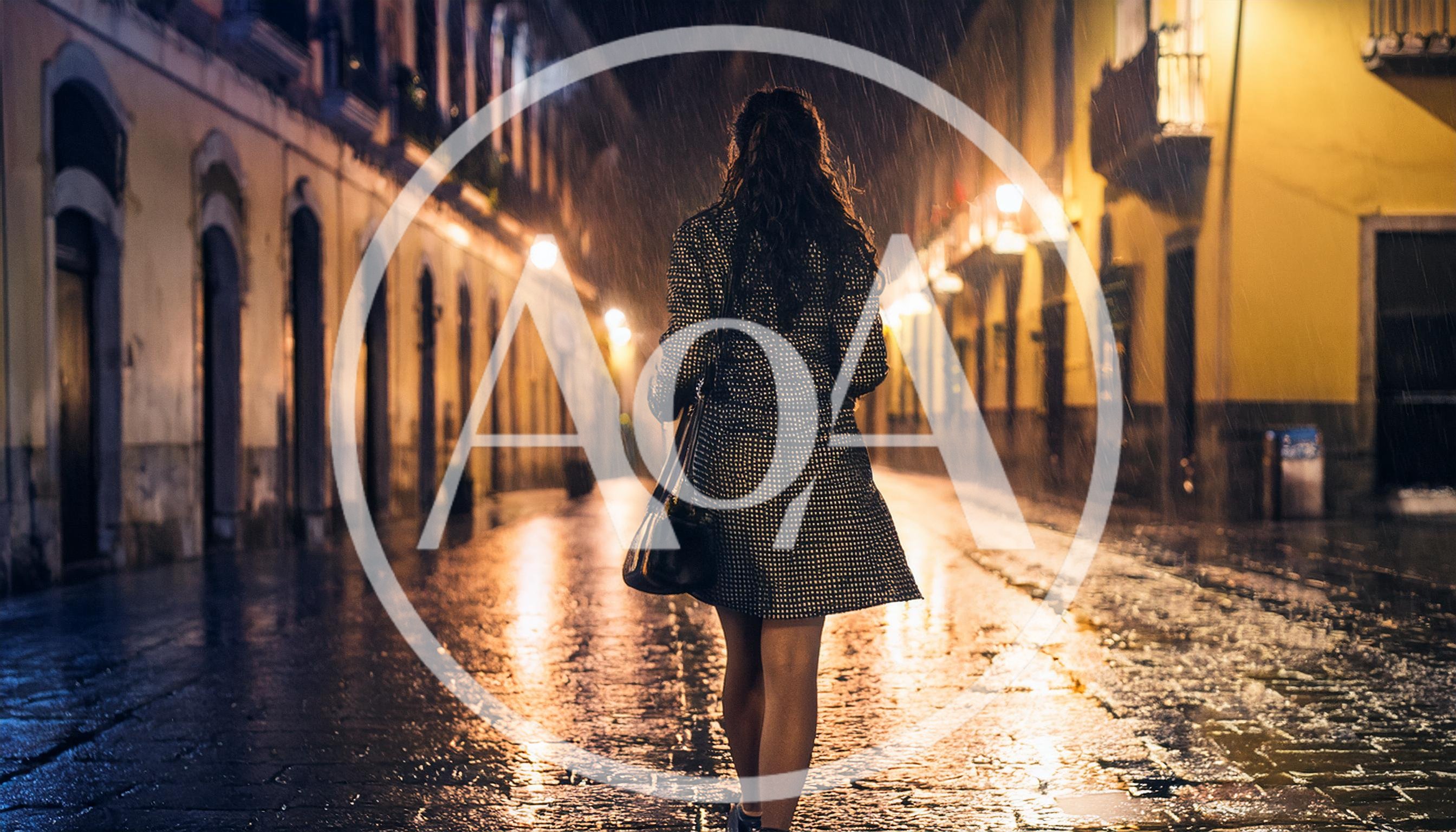 Woman Walking Down A Rainy Cobblestone Street At Night