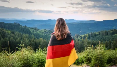 Woman Standing With German Flag Overlooking Forested Mountains