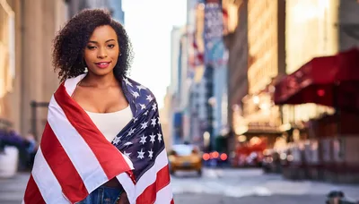 Young Woman Wrapped In American Flag On City Street