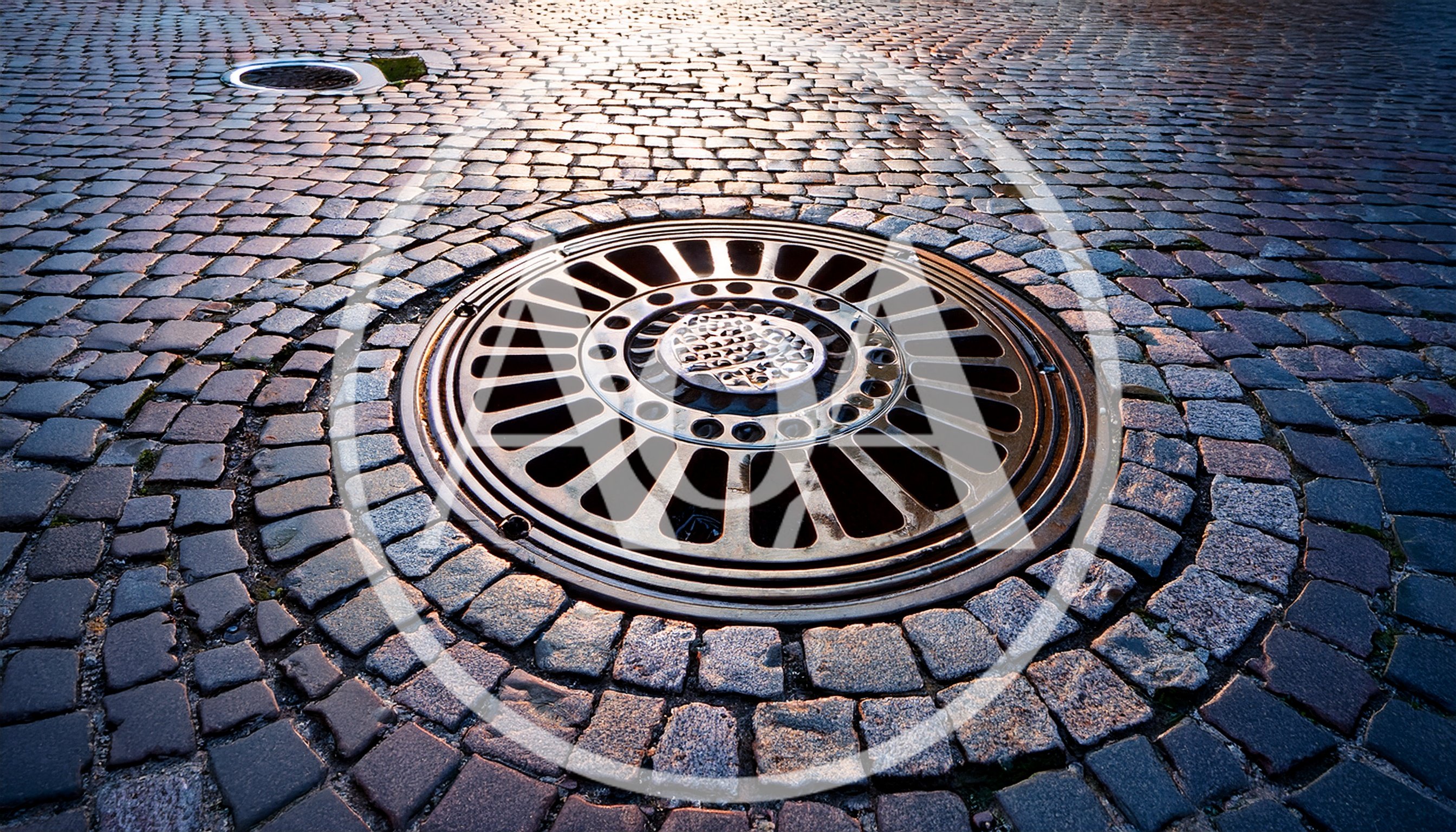 Circular Metal Manhole Cover On Cobblestone Street