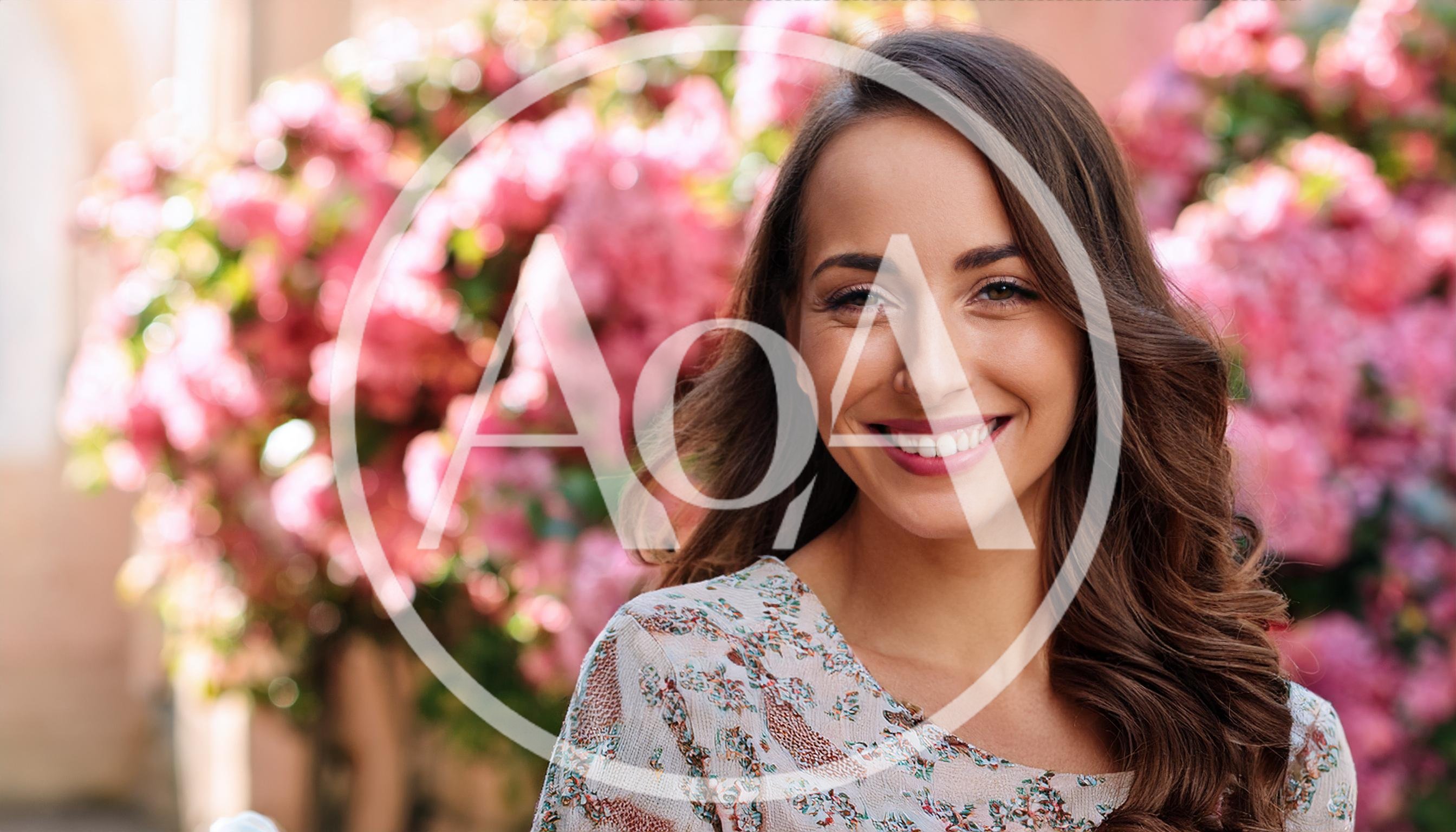 Smiling Young Woman Standing In Front Of Pink Flowers